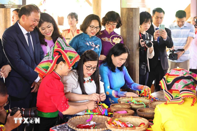 Bà Lê Thị Bích Trân, phu nhân Thủ tướng Phạm Minh Chính trải nghiệm làm quả Còn tại khu nhà dân tộc Thái, Làng Văn hóa-Du lịch các dân tộc Việt Nam. (Ảnh: TTXVN)