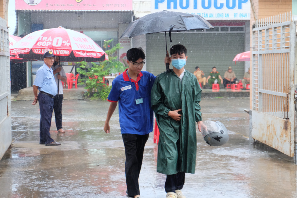 Tình nguyện viên tận tình che dù cho thí sinh trong cơn mưa