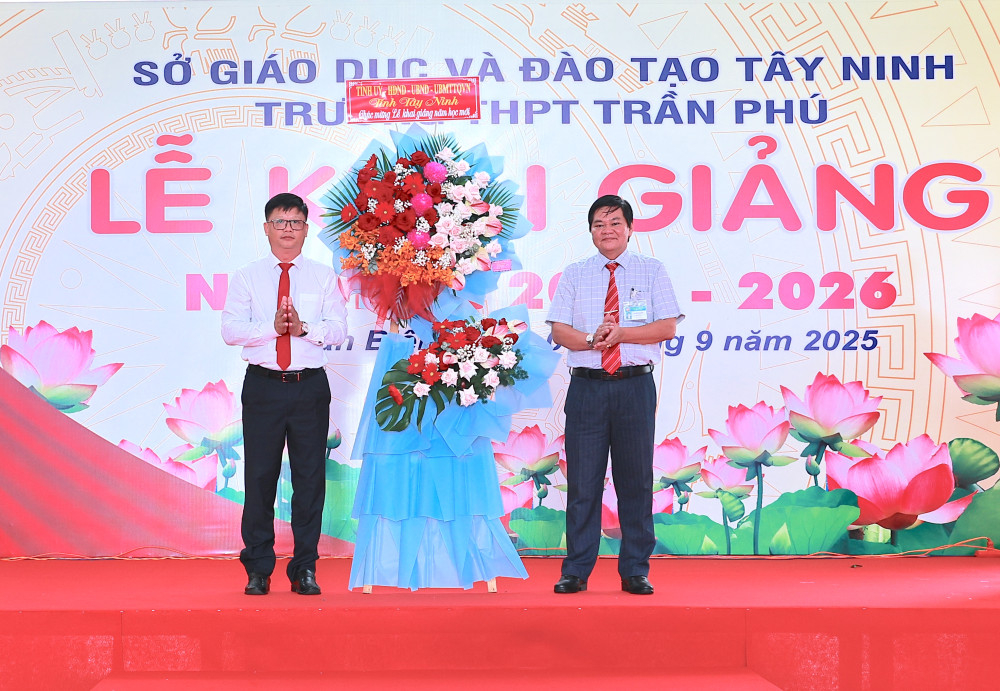Ủy viên Ban Thường vụ Tỉnh ủy, Bí thư Đảng ủy phường Tân Ninh Lê Minh Thế (bên trái) tặng lẵng hoa chúc mừng Trường THPT Trần Phú 